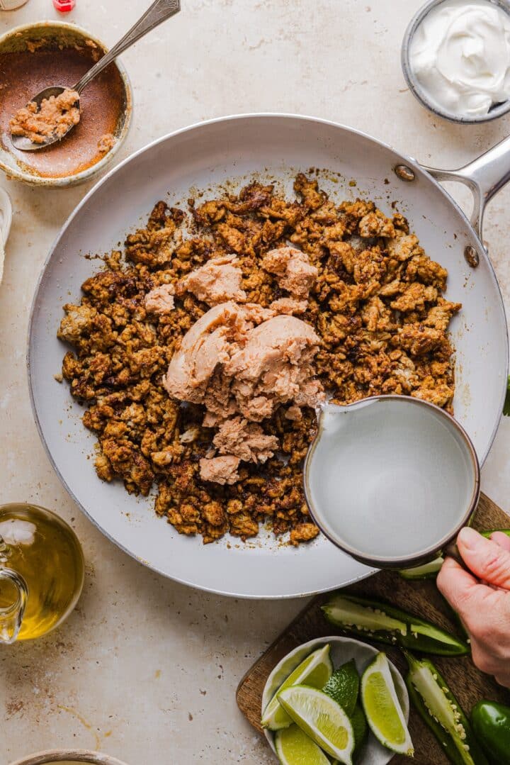 Stirring refried beans and water into cooked turkey in a skillet.