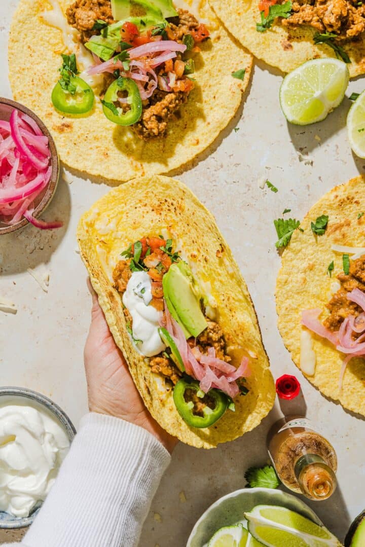 Hand holding a taco filled with seasoned turkey filling and fresh toppings.