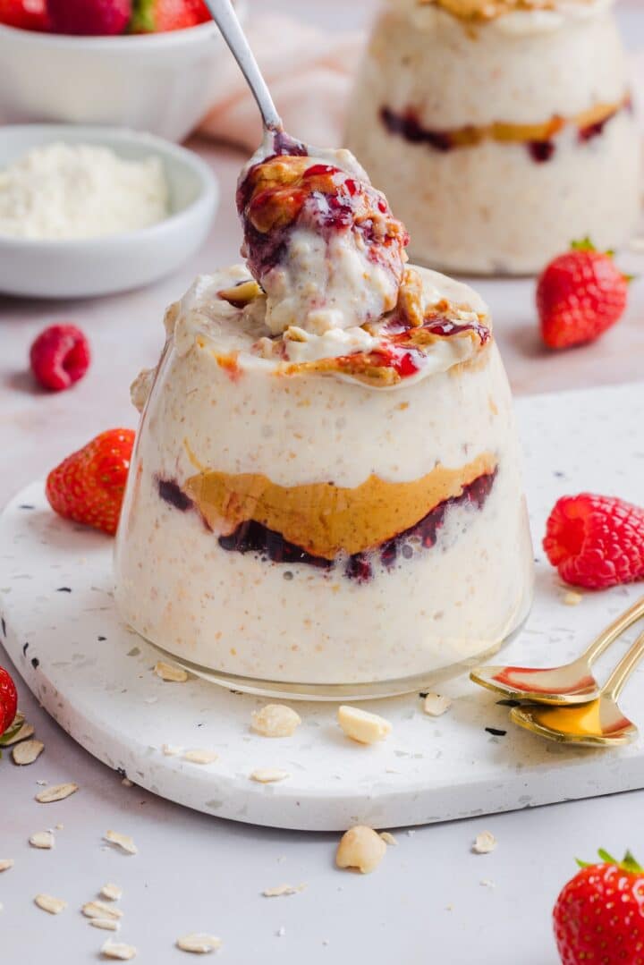 Spoon lifting up peanut butter jelly overnight oats out of a jar.