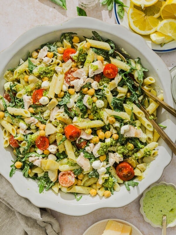Chicken pesto pasta salad tossed on a scalloped white bowl.