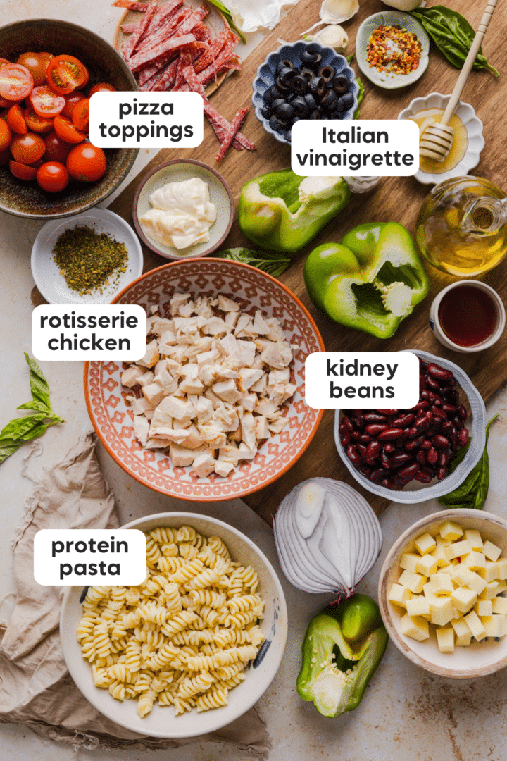 Ingredients for pasta salad including protein pasta, rotisserie chicken, kidney beans, pizza toppings, and Italian vinaigrette.