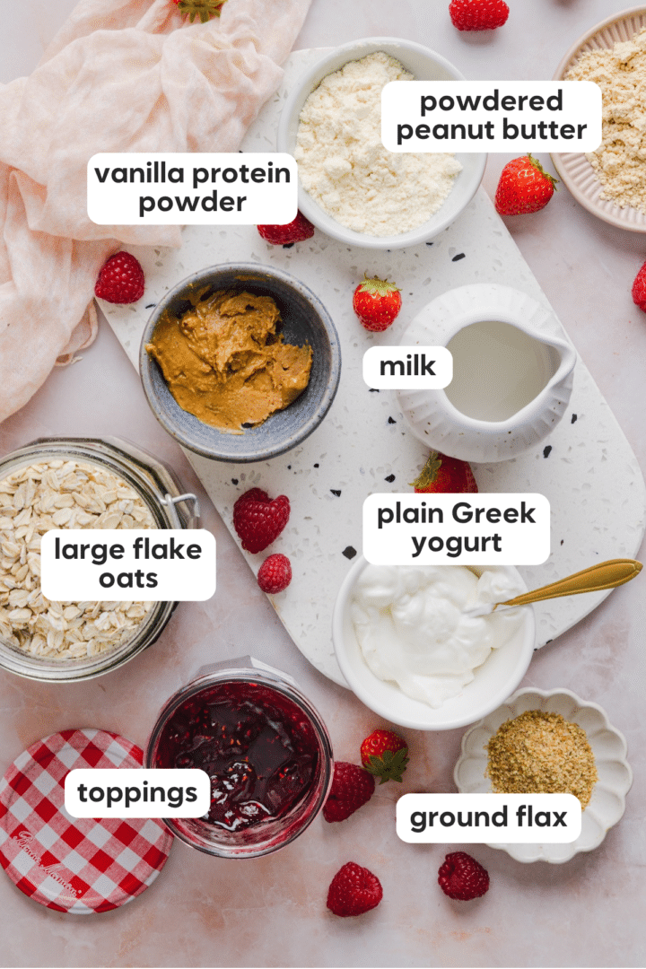Ingredients for overnight oats including plain Greek yogurt, large flake oats, milk, vanilla protein powder, flax, peanut butter and jam.
