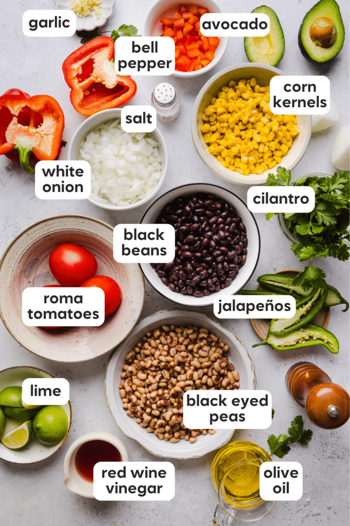 Ingredients for cowboy caviar including black beans, black eyed peas, roma tomatoes, lime, white onion, salt, jalapeños, cilantro, corn kernels.