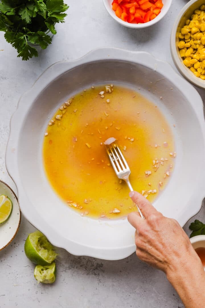 Dressing being whisked in the bottom of a large salad bowl.