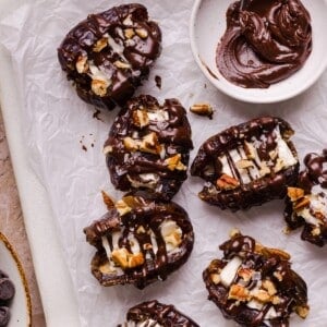 Cream cheese stuffed dates topped with drizzled chocolate on parchment paper.