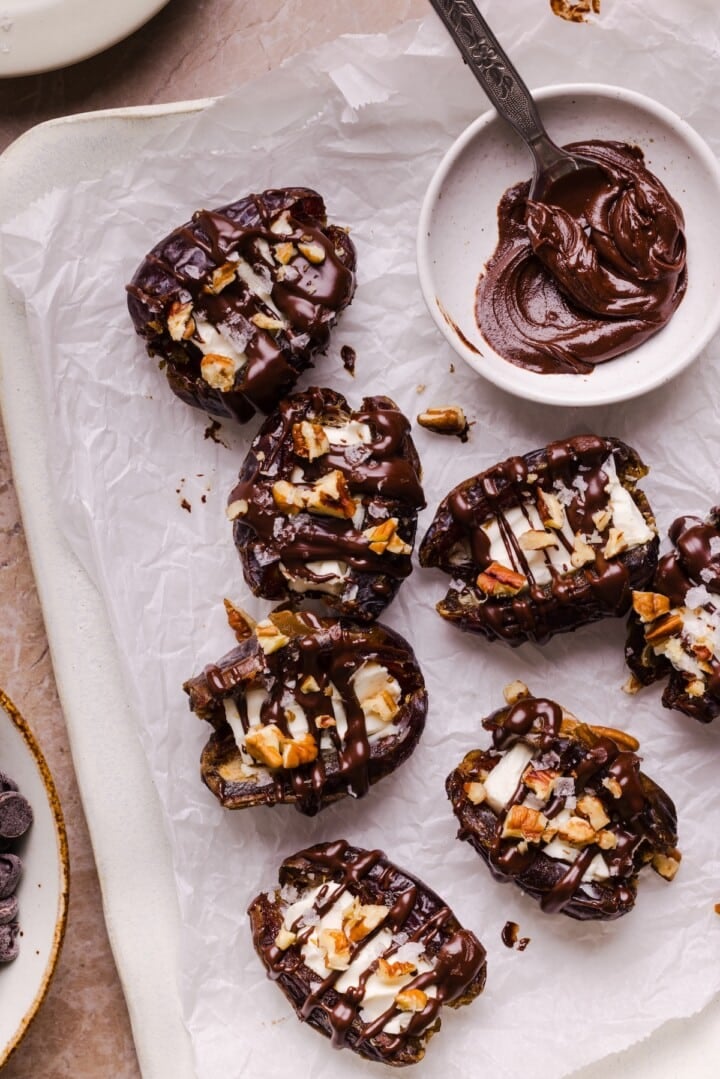 Cream cheese stuffed dates topped with drizzled chocolate on parchment paper.