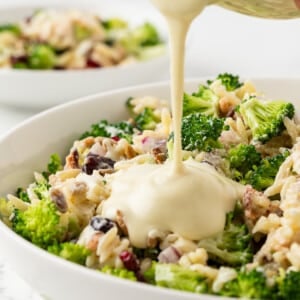 Creamy dressing being poured over broccoli pasta salad.