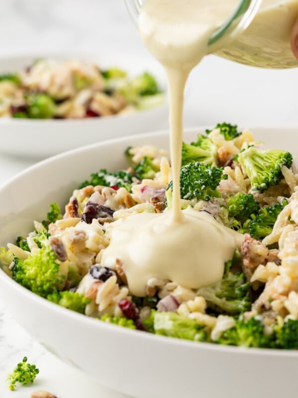 Creamy dressing being poured over broccoli pasta salad.