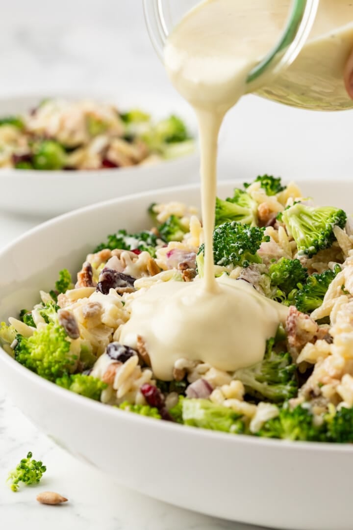 Creamy dressing being poured over broccoli pasta salad.