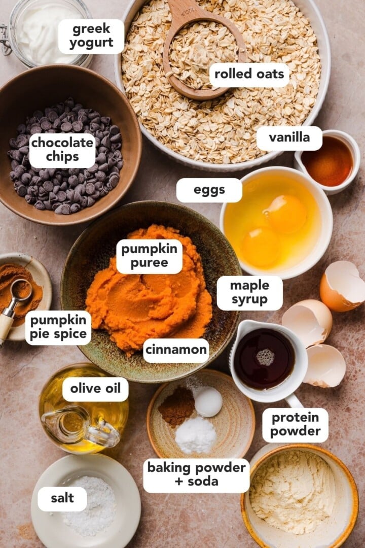 Ingredients for pumpkin protein muffins displayed in small bowls on a kitchen counter.