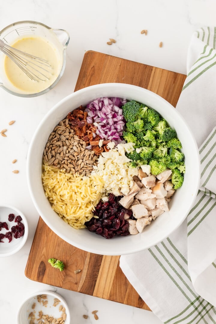 Broccoli pasta salad in a white mixing bowl, unmixed.