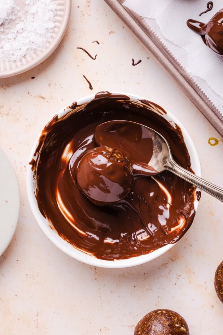 Pecan pie energy bite being dipped into melted chocolate.